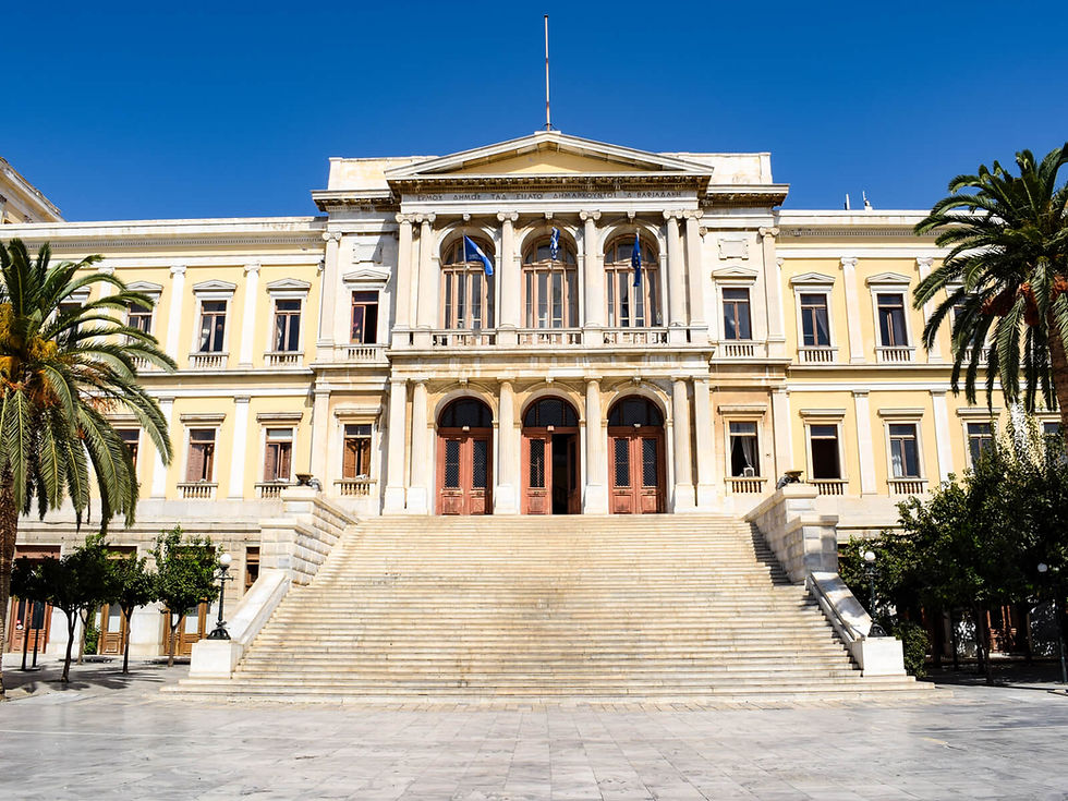 Grand neoclassical building with yellow facade, arched windows, and large stairs. Palm trees frame the scene under a clear blue sky.