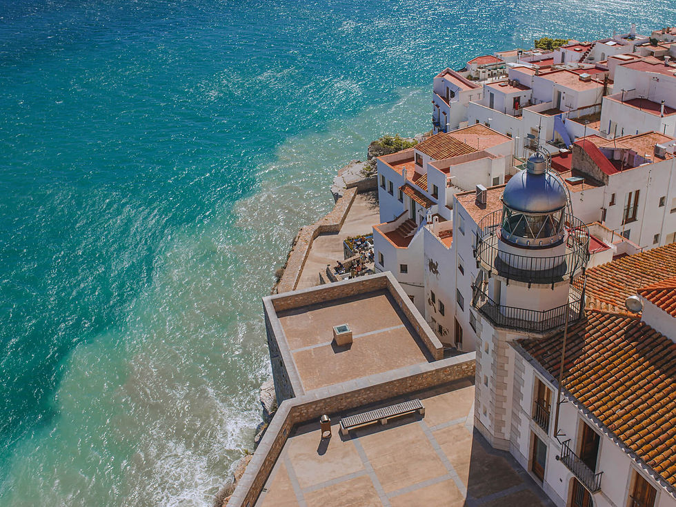 Coastal view with white buildings, red roofs, and a lighthouse by the blue ocean. Sunlit, serene mood, capturing Mediterranean charm.