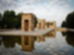Ancient stone temple with reflections in a calm water pool, surrounded by trees. Cloudy sky adds a serene and historic atmosphere.