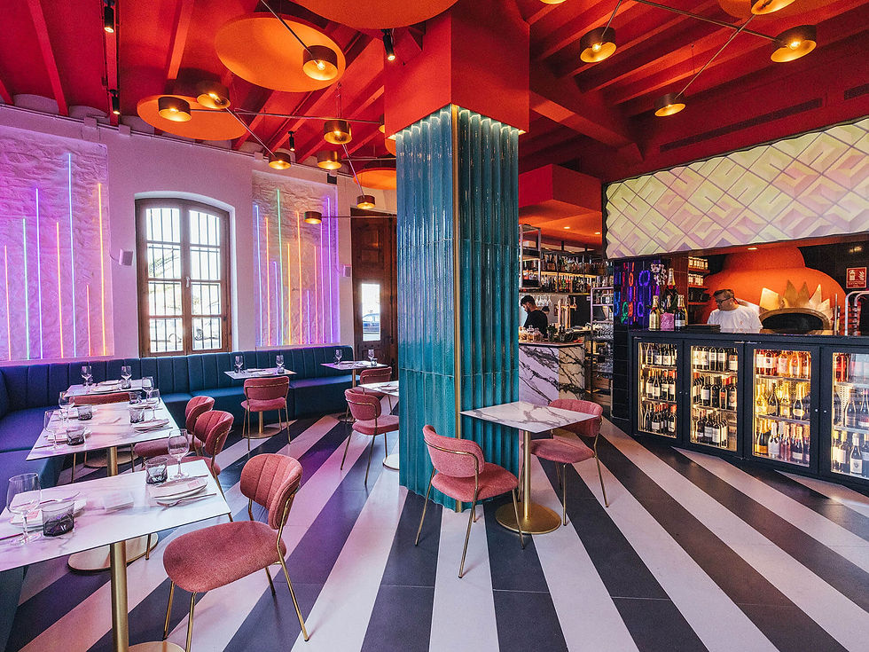 Colorful restaurant interior with striped floor, pink chairs, and neon lights. Chef visible behind the bar. Warm and vibrant ambiance.