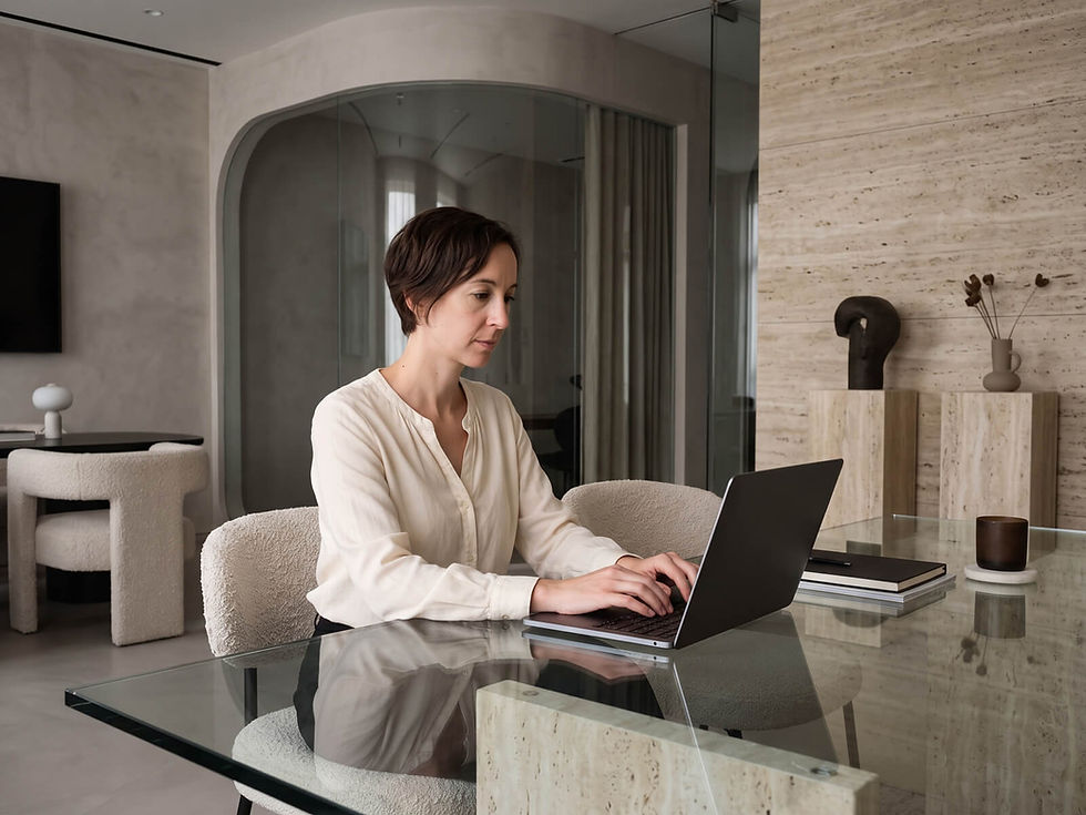 Professional woman typing on a laptop at a glass desk in a modern, neutral-toned office setting.