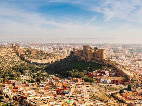 A wide panoramic view of Almería, showing the sprawling city buildings nestled beneath the ancient, fortified walls of the Alcazaba situated on a rocky hill. Header image related to the blog post "The Understated Andalusian City That’s Set for a Revival"