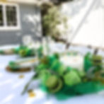 Table with vibrant green and gold settings in an outdoor shaded area.