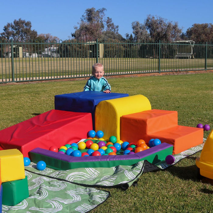 Young child playing with soft play shapes and a ball pit outdoors.