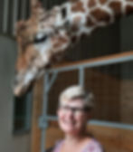 photo of author, short, older, with glasses standing near giraffe in zoo