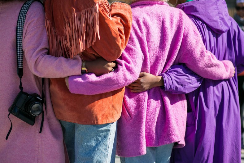 the backs of women in colorful coats hugging
