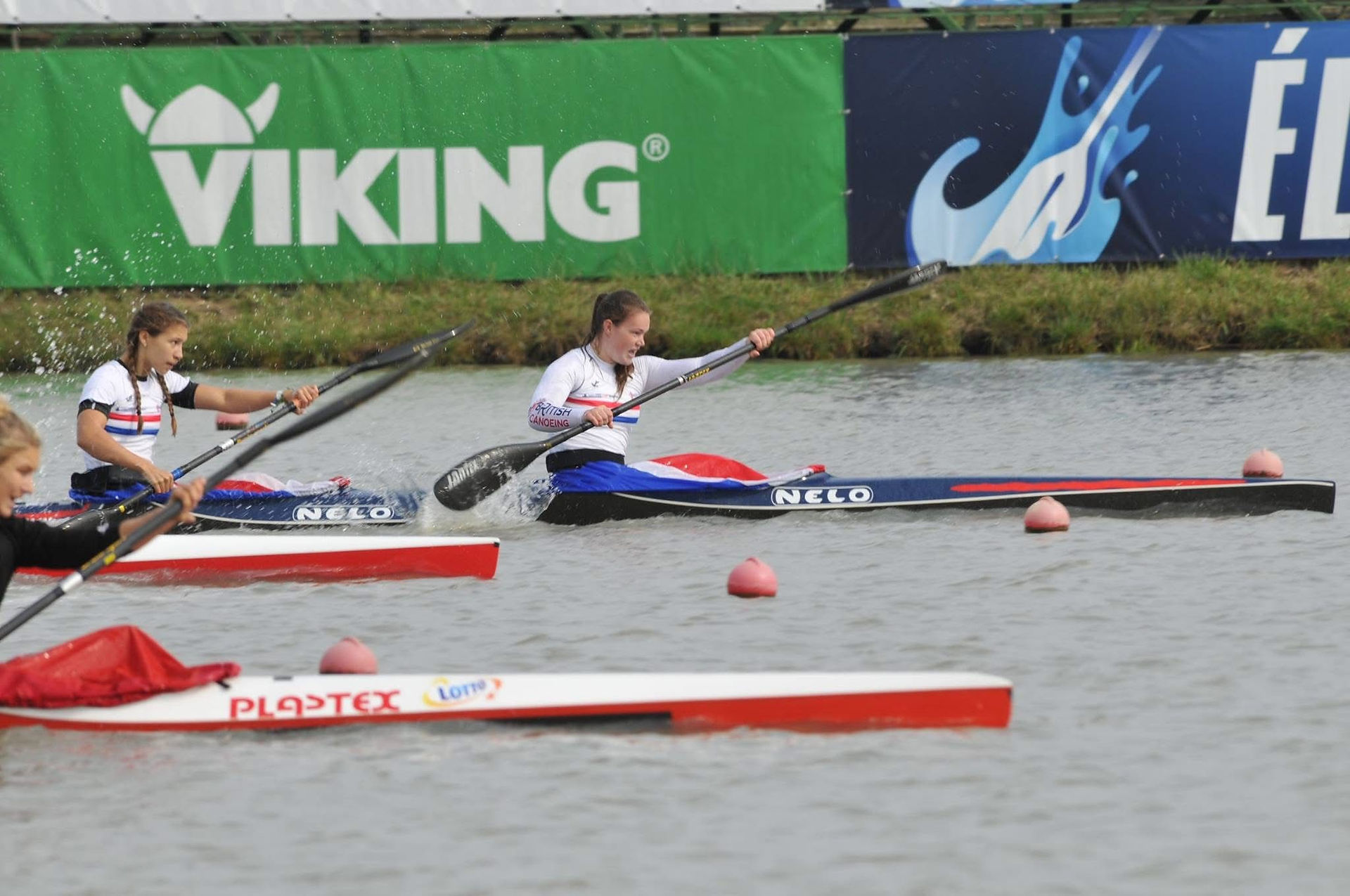Emma Russell paddles in the front seat of a K2 kayak with her teammate. They race down a lane, with the tips of two other boats visible behind them.