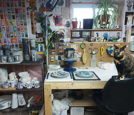 snapshot of ceramic studio table, ceramic work in progress on table, cat sitting on a chair beside it