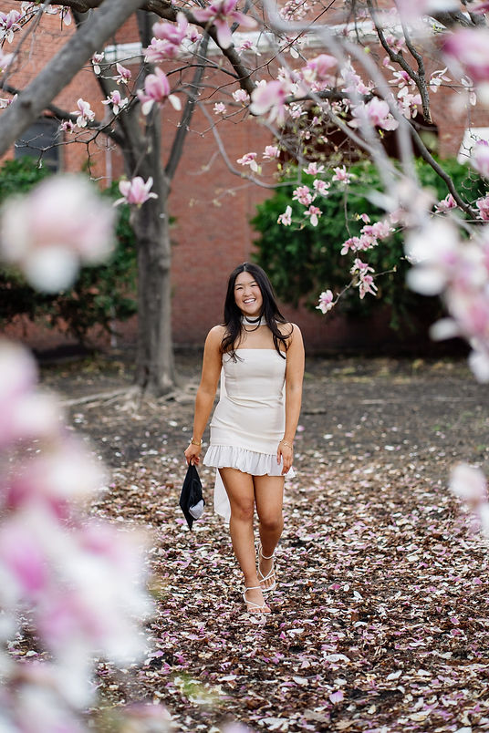Iowa state graduate holding cap walking under a blooming magnolia tree on campus in Ames