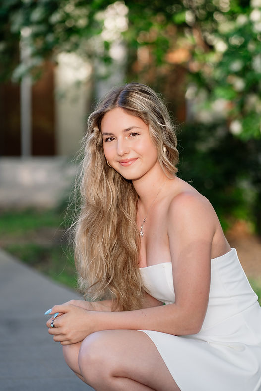 a senior girl squatting on sidewalk looking into the sun
