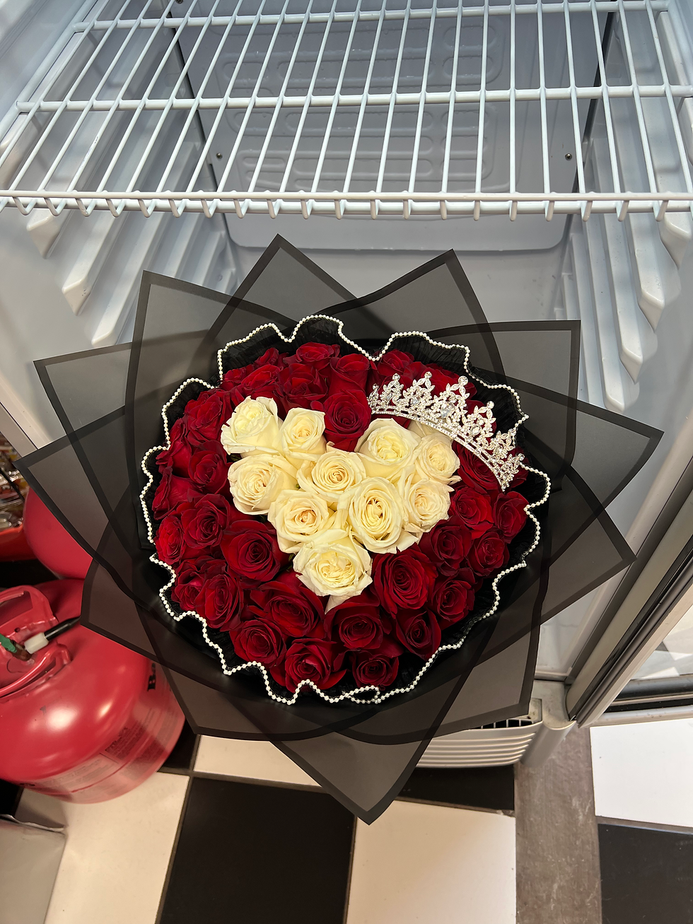 white roses in a heart shape surrounded by red roses, enhanced by a crown decoration and black bouquet wrap
