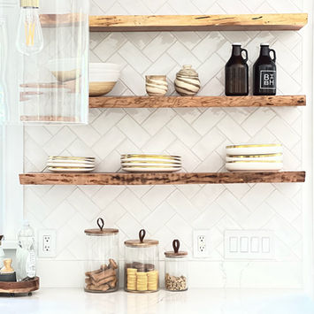 Three live edge floating shelves on a white herringbone tile kitchen wall