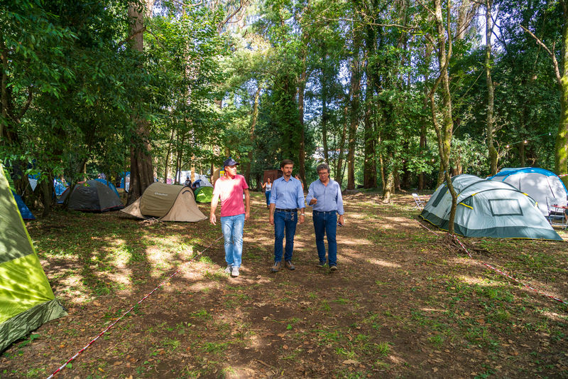 três homens caminhando junto às tendas de campismo