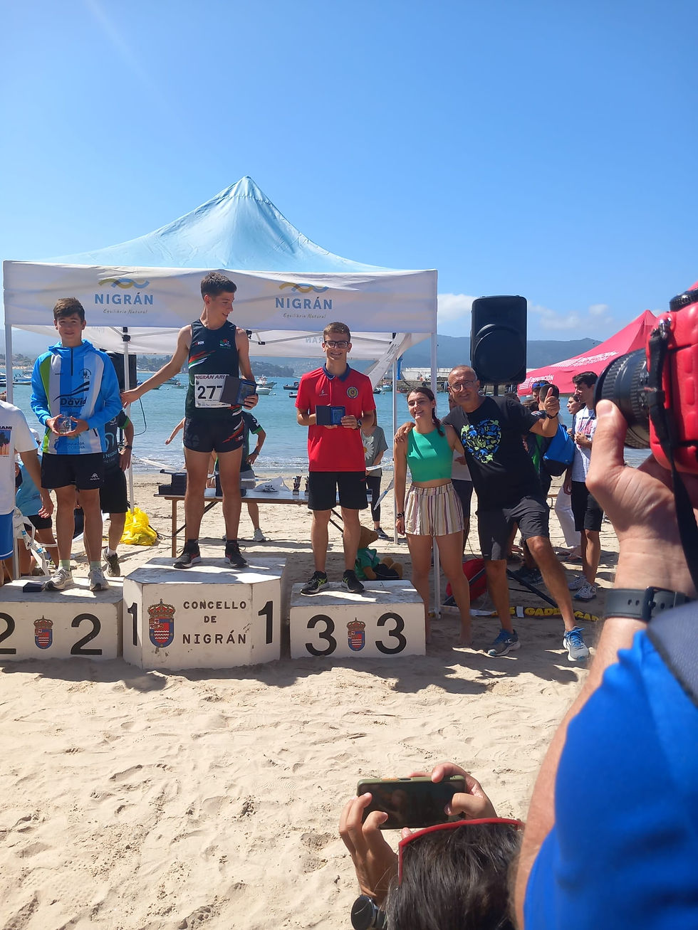 3 jovens no pódio numa praia segurando os prémios