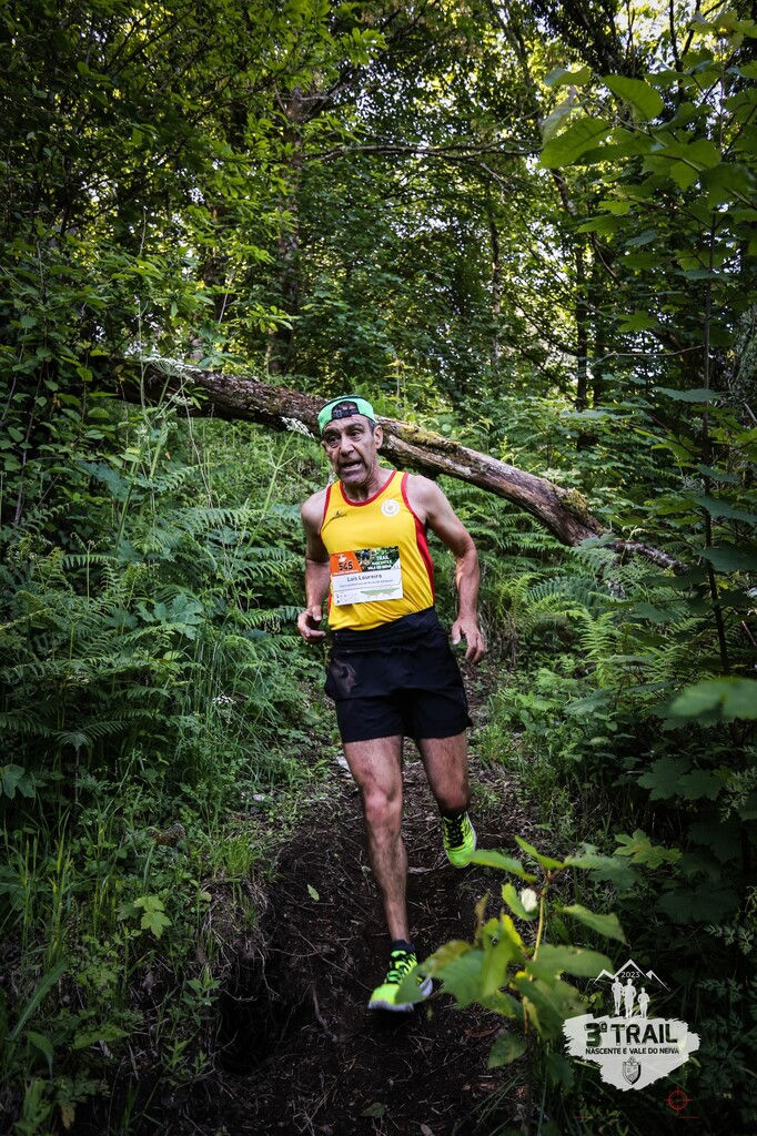 atleta de calções pretos e camisola de cavas amarela correndo por entre arbustos e mato