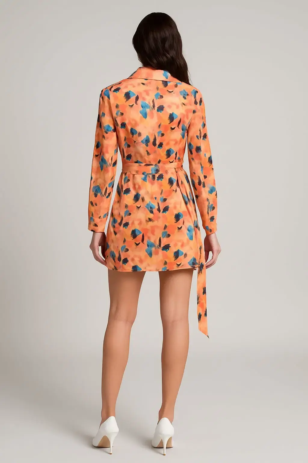 Woman in patterned orange dress, standing; Floral print dress with tie.