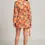 Thumbnail: Woman in patterned orange dress, standing; Floral print dress with tie.