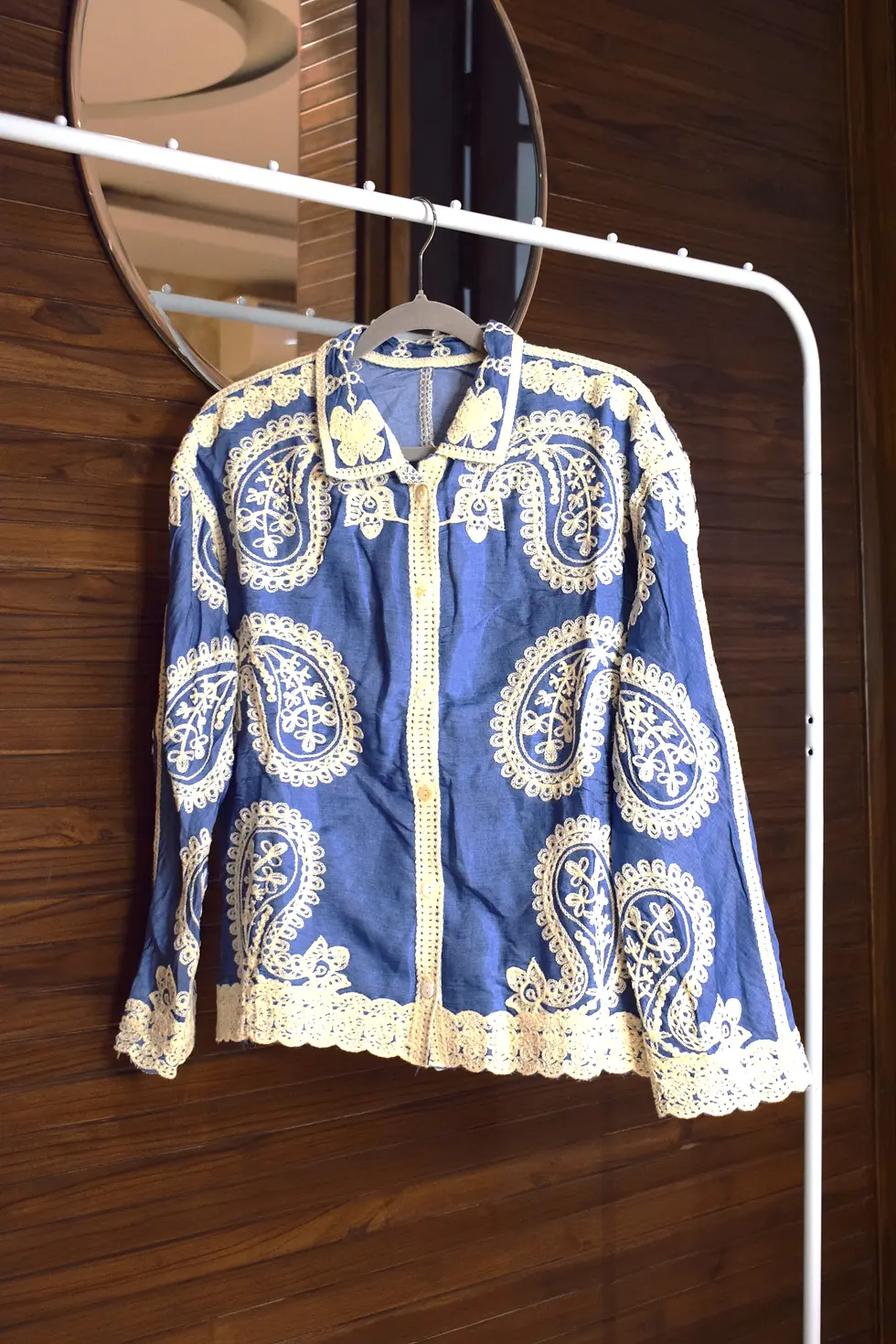 Thumbnail: Blue paisley jacket with white embroidery on a hanger, indoors setting.
