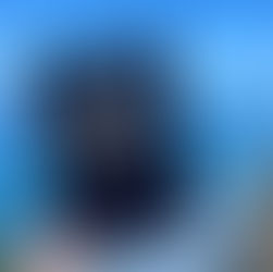 Tablet displaying "The Ascension of Greenville" is held by a hand against a cliffside backdrop with ocean waves and a clear blue sky.