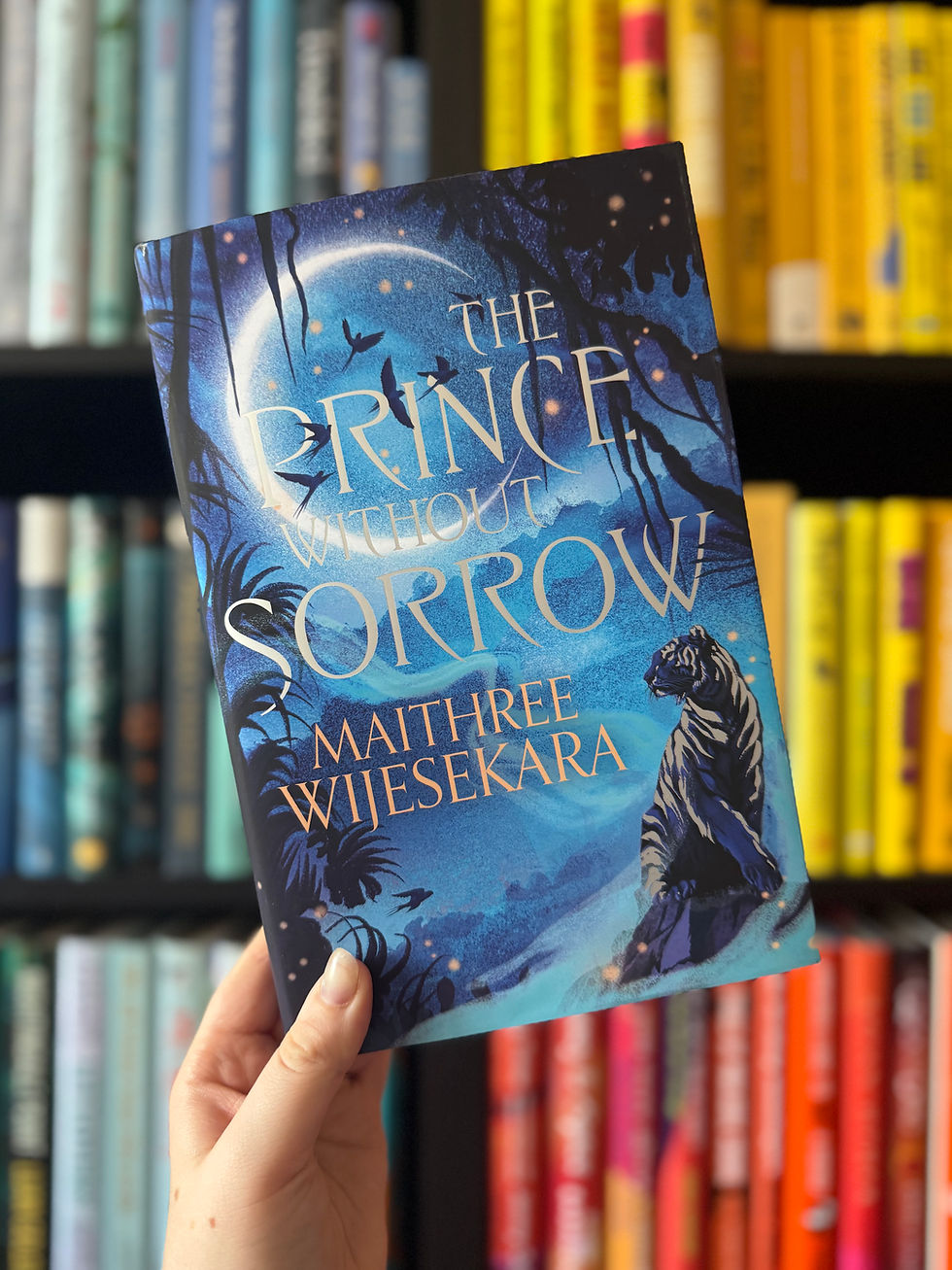 A hand holds a book titled "The Prince Without Sorrow" by Maithree Wijesekara. Cover features blue tones, moonlit scene with a tiger. Bookshelf behind.