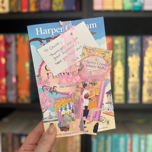 Hand holding a book titled "The Cherry Crush Flower Shop" with a personal note. Colorful bookshelves in the blurred background. Romantic theme.