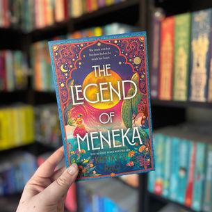 Hand holding colorful book "The Legend of Meneka" in front of a vibrant bookshelf. Elegant cover art features intricate patterns.