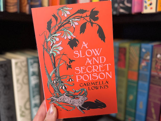 Hand holding an orange book titled "A Slow and Secret Poison" by Carmella Lowkis, with botanical art, in front of a colorful bookshelf.