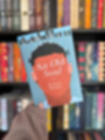 Hand holding the novel "An Old Soul" by M. Kevin Hayden with a colorful bookshelf in the background. The cover features abstract artwork.