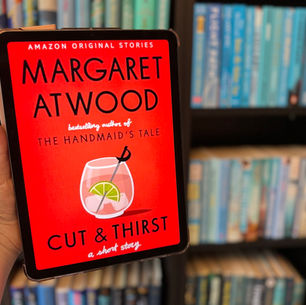 Hand holding a tablet displaying "Cut & Thirst" by Margaret Atwood. Red cover with a cocktail image. Blurred bookshelf background.