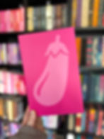 A pink card with an eggplant graphic is held in front of colorful bookshelves. The vibe is playful and vibrant.