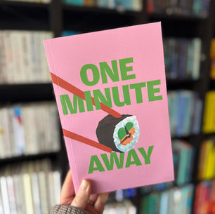 Hand holds a pink book titled "One Minute Away" with a sushi illustration, against a blurred bookshelf background.