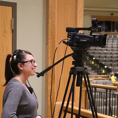 Woman standing behind a camera in an auditorium.