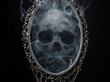 smoky image of a skull inside an ornate, silver hand mirror