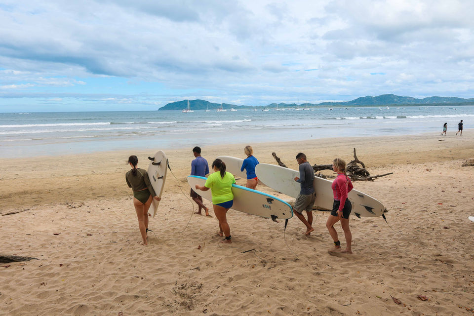 Group of surfers with their boards heading to the water on a beach in Costa Rica
