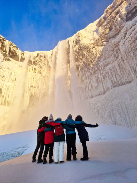 solo travelers embracing as they watch an icy waterfall in Iceland