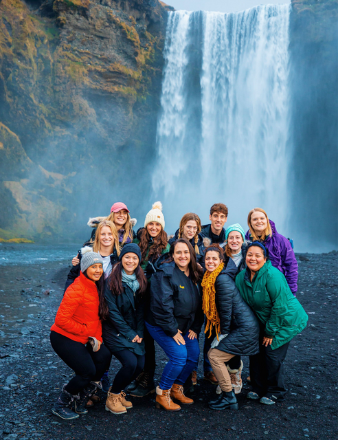 Group travelers in colorful jackets in front of a large waterfall in Iceland.