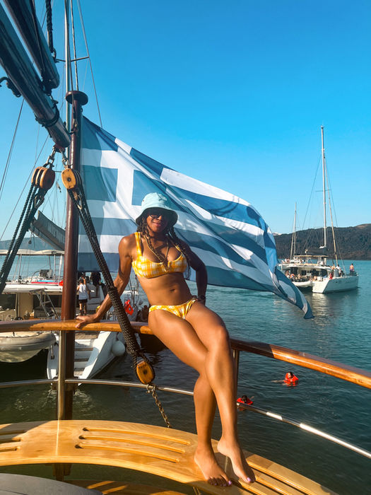 Solo traveler posing on a boat with the Greek flag waving in the wind.