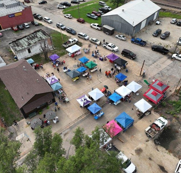 Aerial view of the Kids Farmers Market at A Station in downtown Abilene, Kansas, featuring dozens of youth vendor booths, shoppers and colorful tents during a community market.