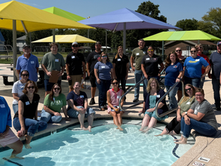 Do-Alogue participants gather around the shallow end of the Solomon Municipal Pool beneath colorful shade structures.
