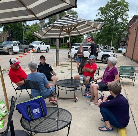Community members gather under patio umbrellas outside A Station during the Kids Farmers Market in Abilene, visiting and supporting local youth entrepreneurs.