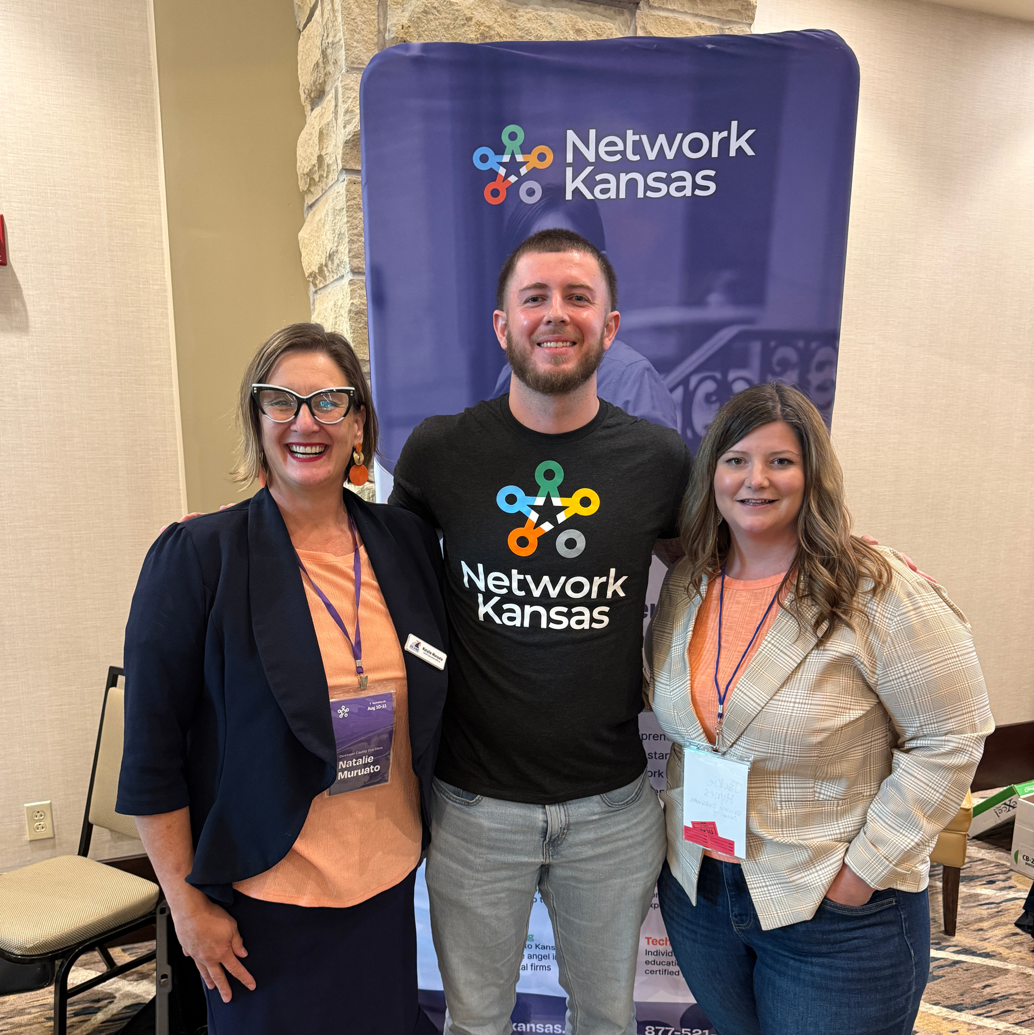 Natalie Muruato, Dyelan Reed and Jackie Hynes stand together in front of a Network Kansas display at the Kansas Entrepreneurship & Youth Summit.