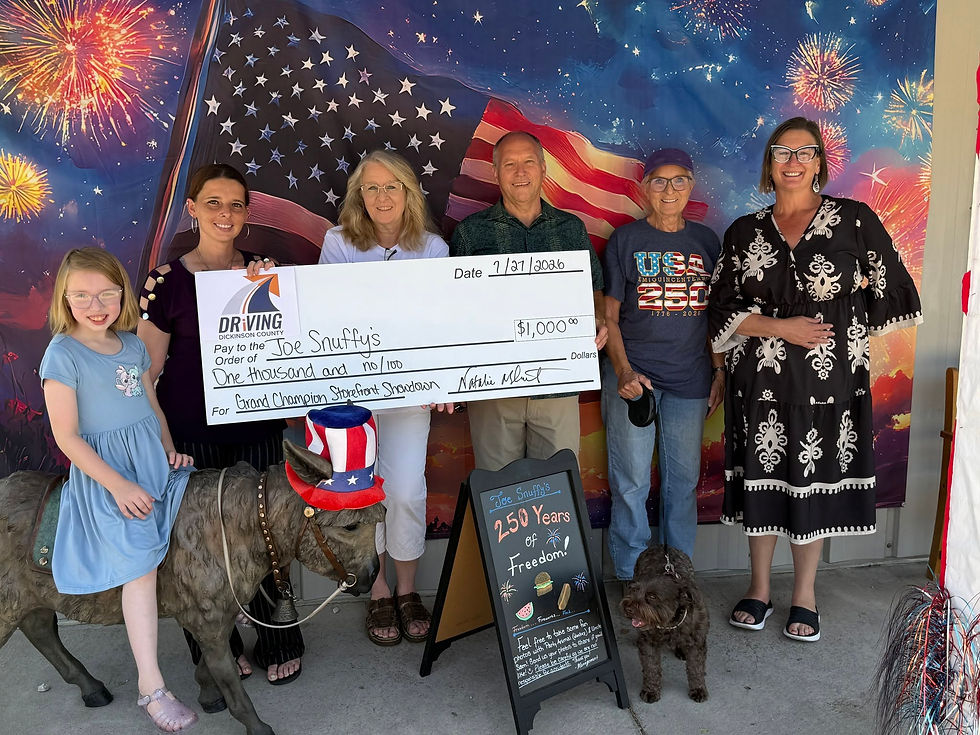 Joe Snuffy's owners, staff, and family hold an oversized $1,000 Grand Champion check in front of a patriotic fireworks backdrop, alongside Libby the donkey statue dressed in a stars-and-stripes top hat.