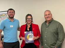 Three members of Dickinson County’s eCommunity partnership stand together indoors, with the person in the center holding a Network Kansas annual report.