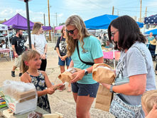 Seven-year-old Hailey talks with customers at her farmers market booth as they purchase locally made and grown products.