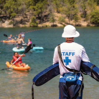 A lifeguard, labeled as 'Aquatic Center Staff', oversees kayakers and paddleboarders enjoy