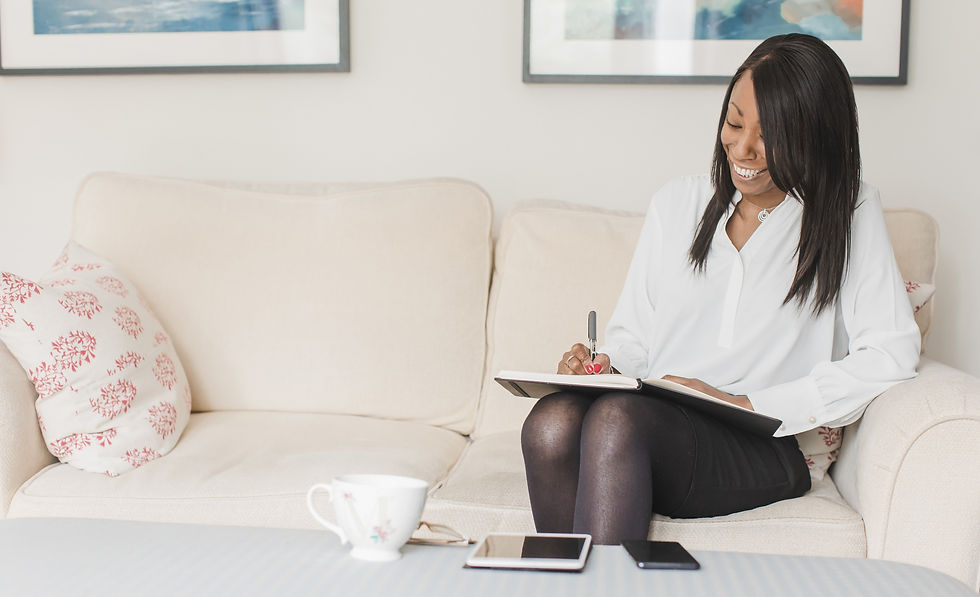 Melanie Marshall sitting on a white sofa, smiling and writing in a notepad