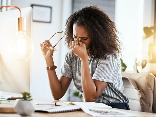 a woman is pinching her nose in stress in front of a copputer with bills on the table.