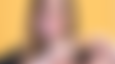 A woman with a soft smile posing with her hands shaping a heart whilst wearing a Let's Keep the Ball Flying merchandise. Background is yellow.