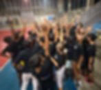 Large group of young volleyball players gathered on the side of a volleyball court celebrating with their arms up in the sky during a VoleiPaz session in Cali, Colombia