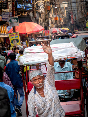 mož v svetli srajci vozi rdečo rikšo in dviga levo roko v pozdrav